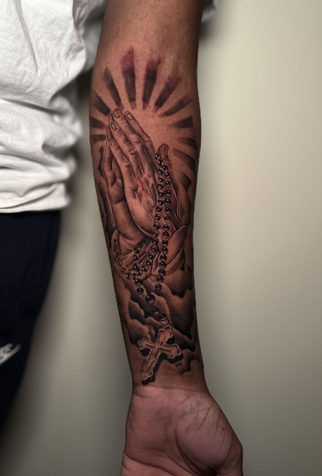 Praying hands with rosary and sun rays forearm